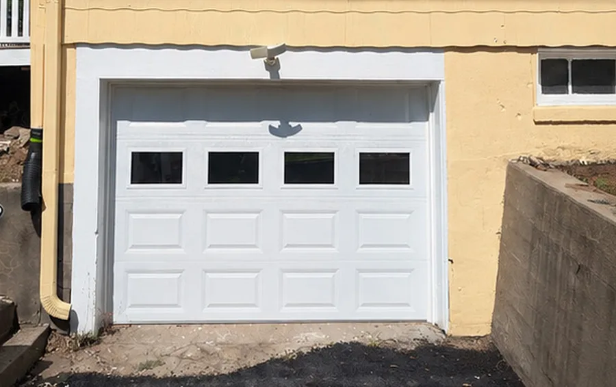 New white raised-panel garage door with window sections after replacement